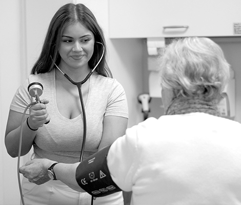 Eine Medizinische Fachangestellte (MFA) misst den Blutdruck einer Patientin mit einem Stethoskop